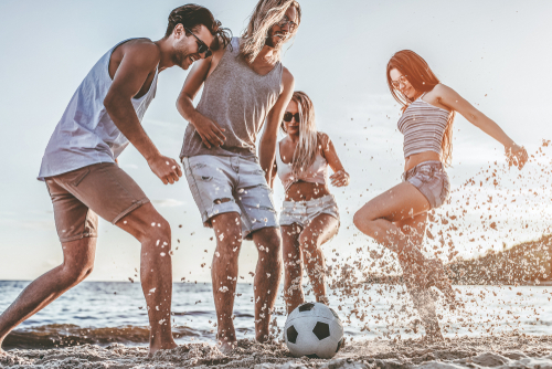 4 Freunde, männlich und weiblich spielen am Strand im Meer - Wasser Fußball.