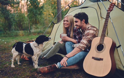 Blonde Frau und dunkelhaariger Mann campen im Wald mit Hund.