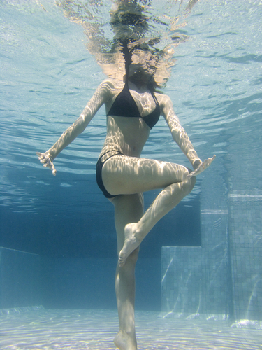 Frau die im Schwimmbecken steht und unter Wasser Aquafitness und Wasserqymnastik macht.