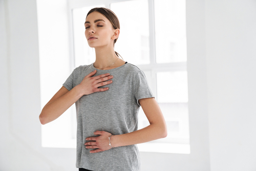 Frau, die eine Hand auf ihre Brust und eine auf den Bauch legt. Tief ein und ausatmen.