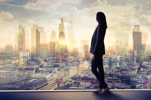 Business Frau steht vor einem großen Fenster und schaut in die Stadt.