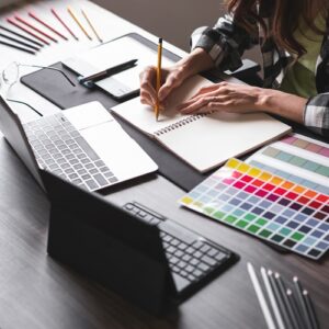 Grafikerin, die mit Grafikdesign Ausstattung am Schreibtisch sitzt und mit einem Stift schreibt.