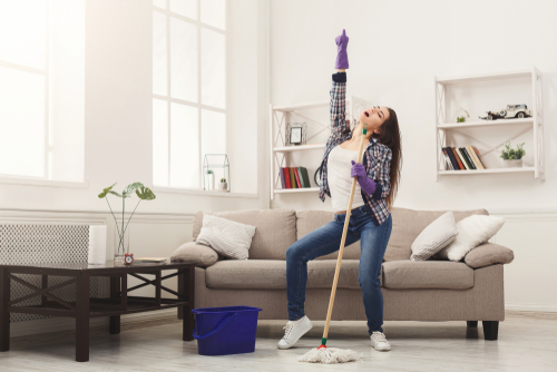 Frau steht im Wohnzimmer mit Mop und Eimer, sie macht sauber, singt und tanzt