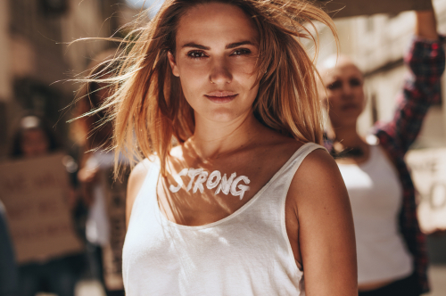 Blonde Frau ist bei Demo, auf ihrer Brust steht das Wort Strong in weißen Buchstaben.