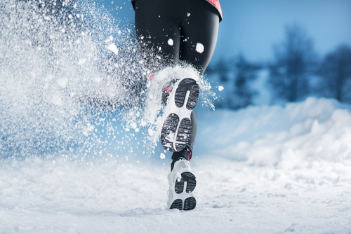 Training im Winter. Eine Frau joggt bei Schnee, Eis und Kälte.