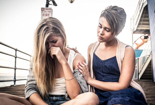 2 Frauen sitzen auf einer Treppe, eine der beiden weint während die andere sie tröstet.