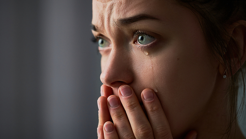 Frau weint und hält erschüttert die Hände vor dem Mund. Tränen laufen über die Wange