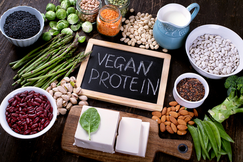 Auf einer kleinen Tafel steht Vegan Protein, daneben liegen Gemüse, Tofu, Nüsse und Hülsenfrüchte