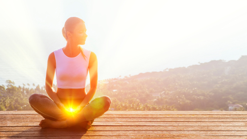 Frau sitzt in Meditationshaltung, ihr Wurzelchakra strahlt hell leuchtend.